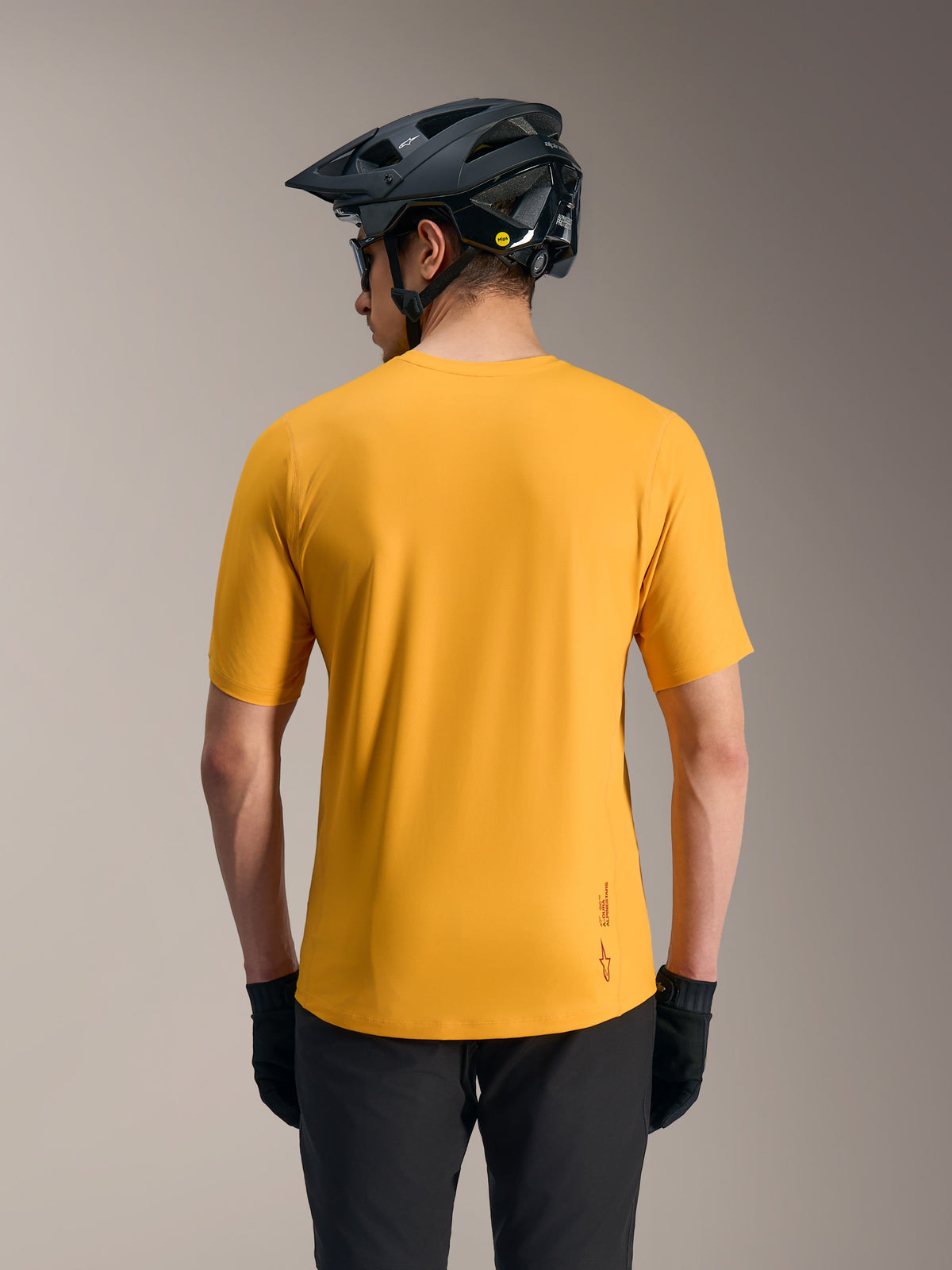 Camiseta Alpinestars A-Dura Ride naranja, jersey ligero de MTB con logotipo y cola larga, vista trasera con casco.