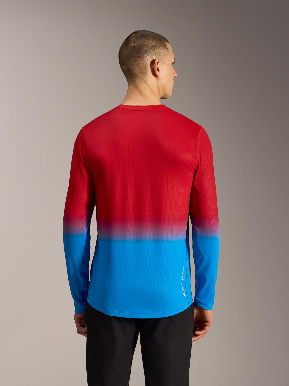 Vista posterior de la camiseta Alpinestars A-Dura ASTARS 2.0, diseño degradado rojo y azul con corte trasero extendido.