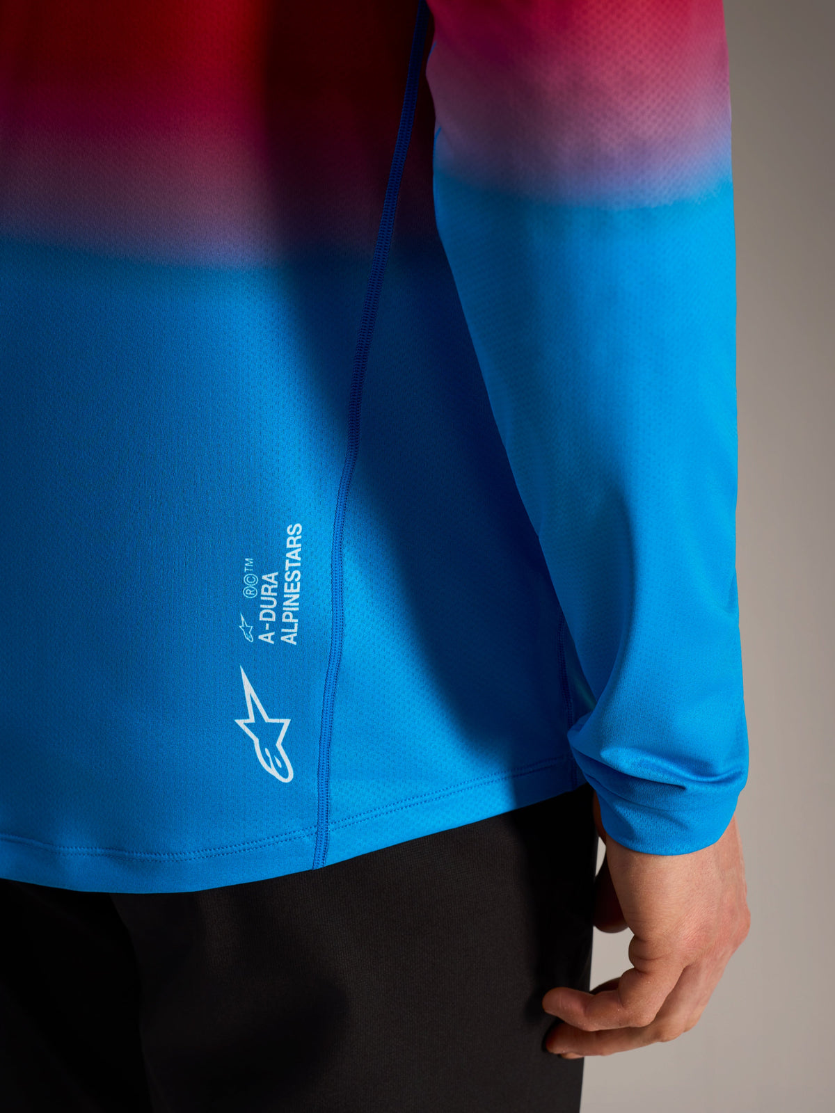 Camiseta A-Dura ASTARS 2.0 de manga larga con degradado rojo y azul y logotipo blanco de Alpinestars en el lateral.