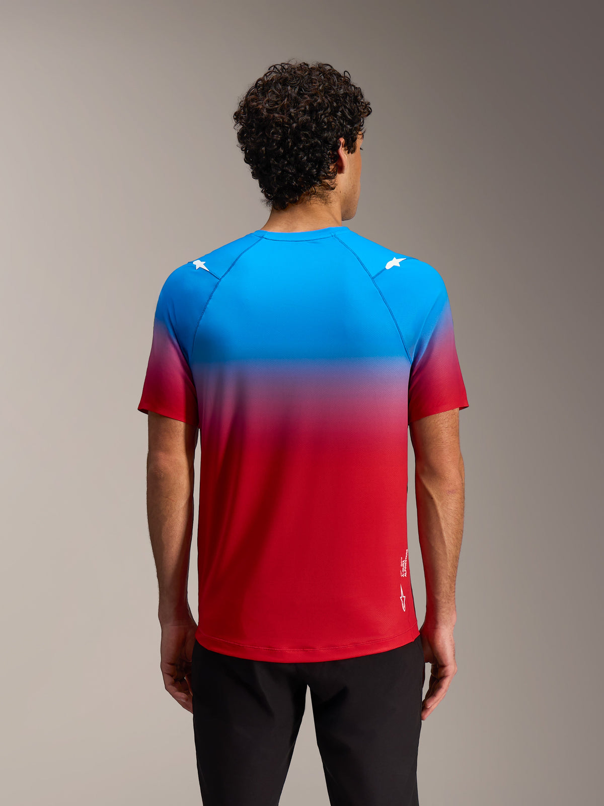 Maillot Alpinestars A-Dura ASTARS 2.0, manga corta, degradado rojo y azul con logos en los hombros, vista trasera.
