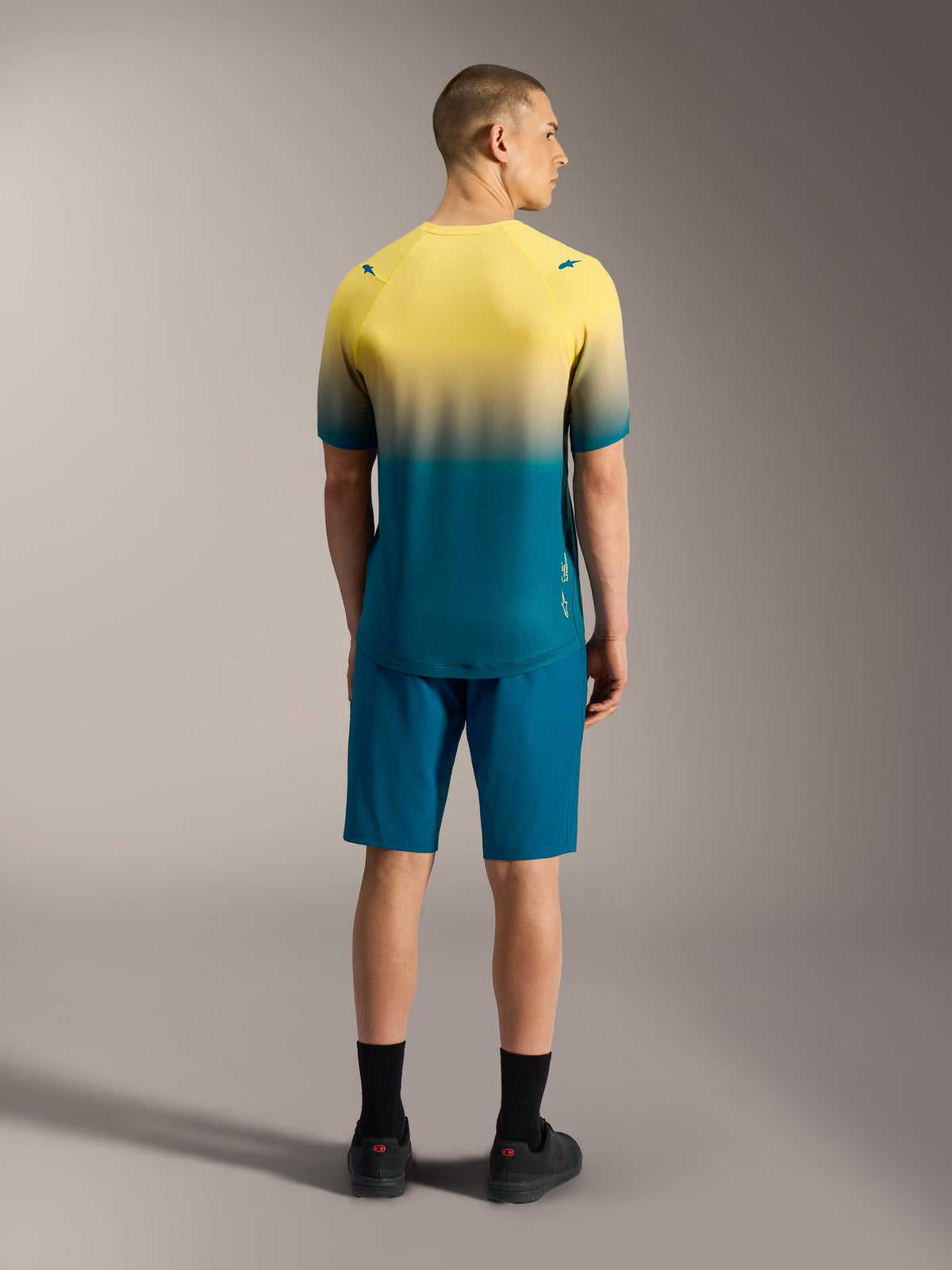 Maillot A-Dura ASTARS 2.0 de manga corta, degradado amarillo a verde azulado, vista posterior sobre modelo
