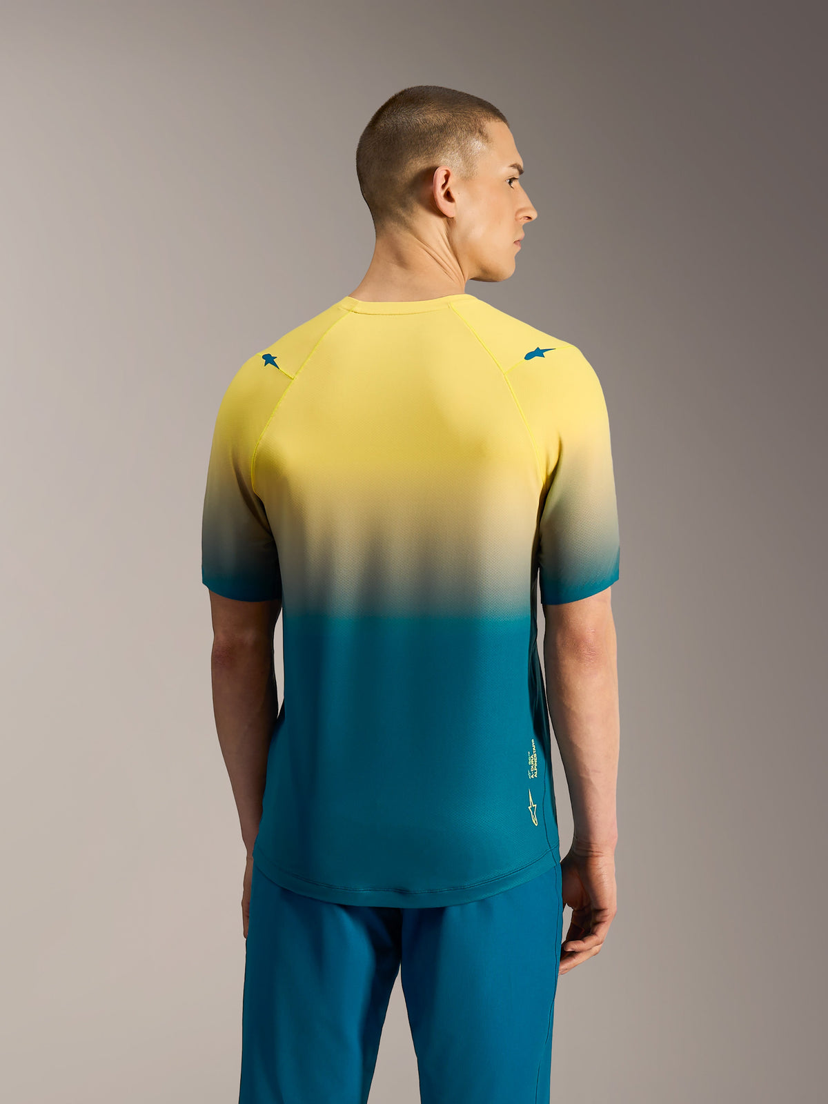 Maillot A-Dura ASTARS 2.0 de manga corta con degradado amarillo y azul verdoso, prenda de alto rendimiento vista desde atrás.