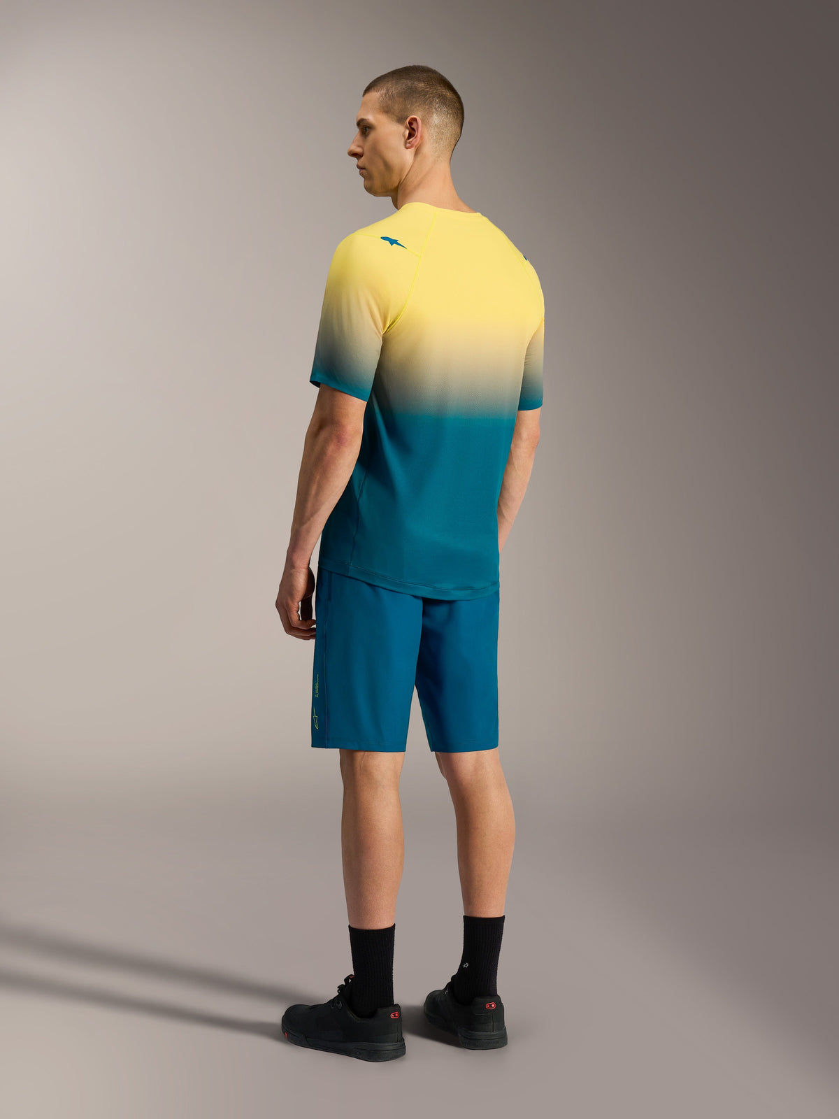 Maillot A-Dura ASTARS 2.0 de manga corta en degradado amarillo y verde azulado con shorts azules de alto rendimiento.