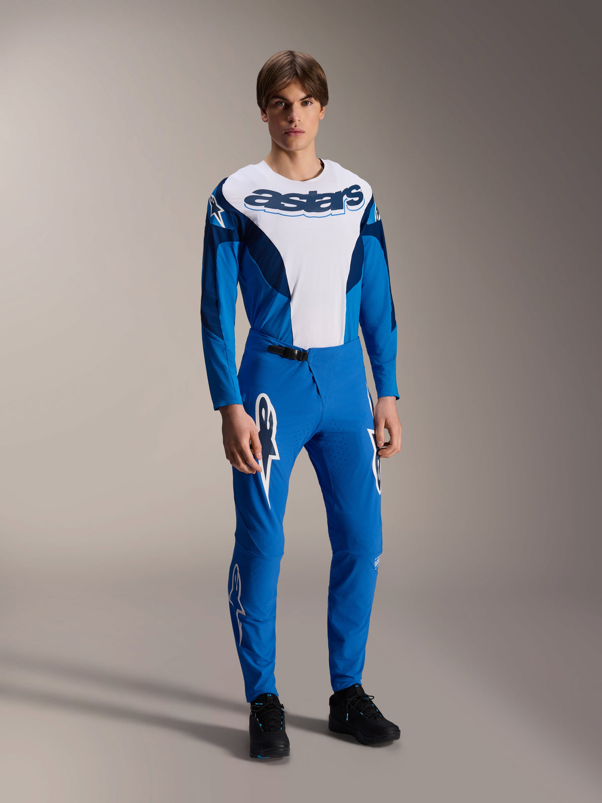 Model wearing complete Alpinestars MTB racing gear, blue and white long-sleeve jersey with 'astars' branding, matching blue A-Supra Melt pants with white star logos, professional mountain bike apparel for off-road riding