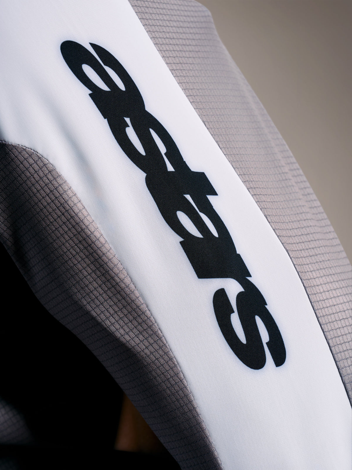 Detalle del maillot A-Supra Elite, tejido microperforado Faded Gray con logo ASTARS negro sobre banda blanca de la manga.