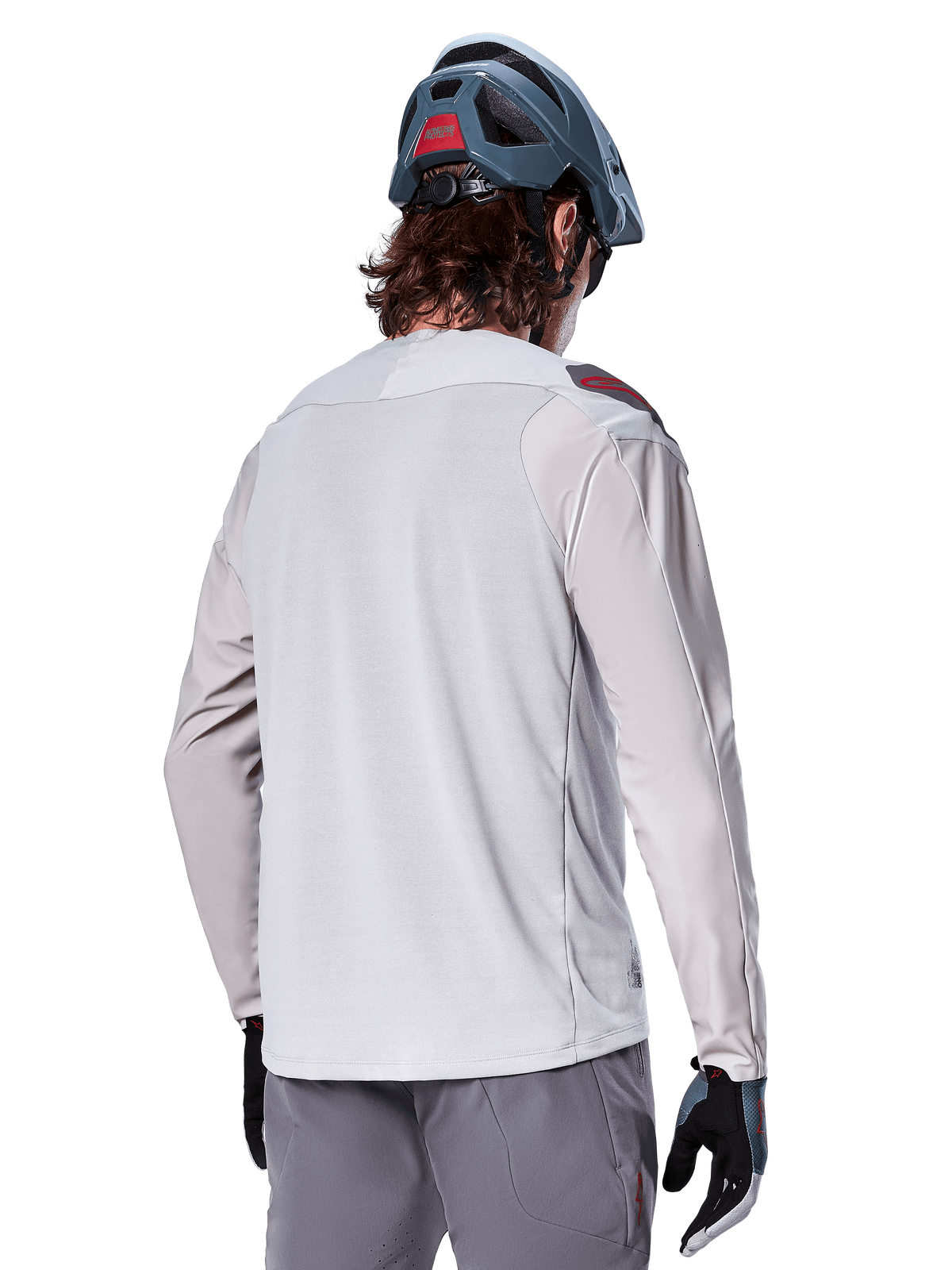 Jersey de manga larga Alpinestars A-Aria Polartec Switch, gris claro, visto desde atrás en un ciclista, usado con un casco de montaña azul y pantalones grises, ropa de rendimiento para ciclismo de montaña en senderos todoterreno