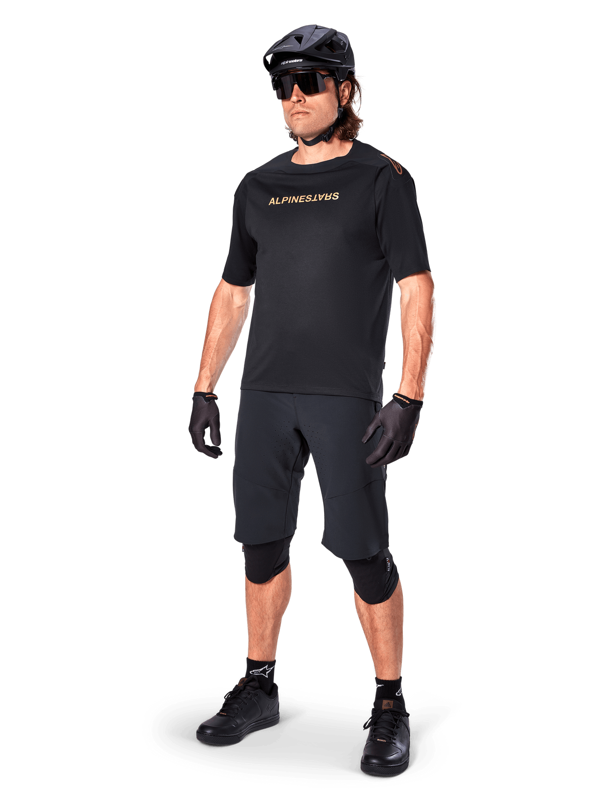 Alpinestars A-Aria Polartec Switch Short Sleeve Jersey, Black, featuring mirrored gold chest branding, worn by a rider with black cycling shorts, helmet, and knee pads, technical MTB gear for off-road performance