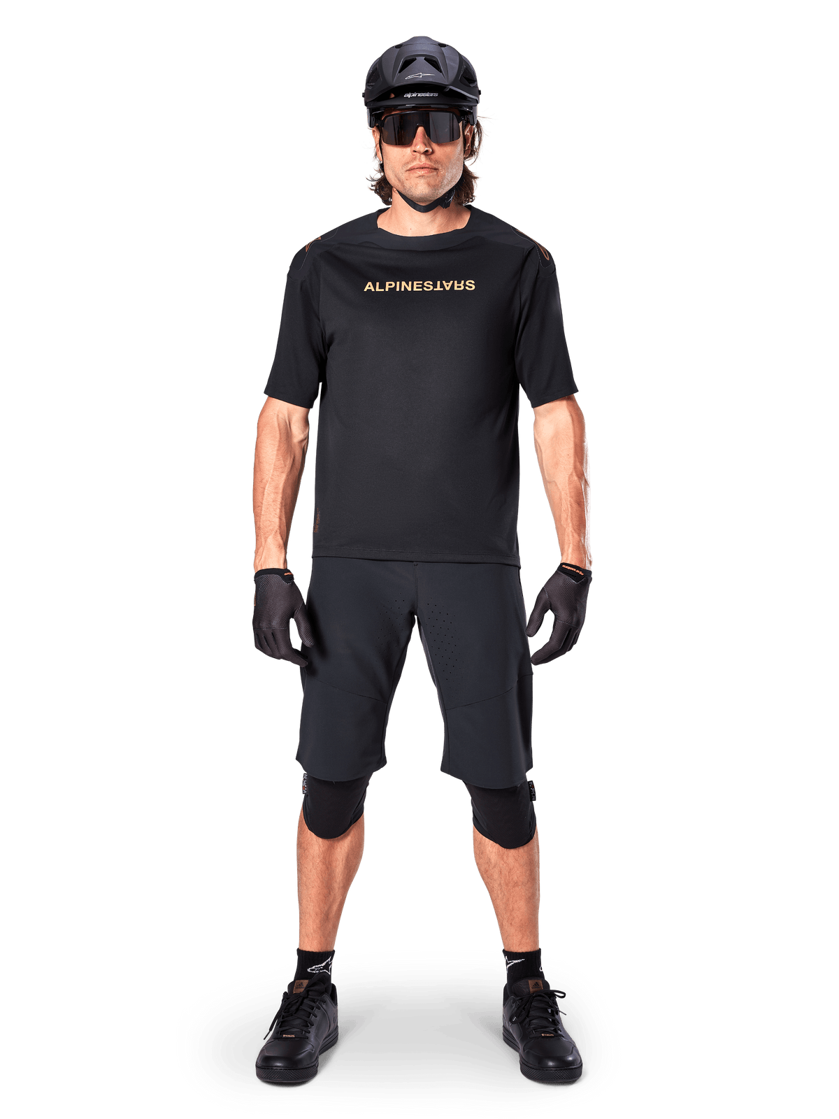 Alpinestars A-Aria Polartec Switch Jersey, Short Sleeve MTB Jersey, Black with tan lettering, worn with coordinated black mountain bike gear including helmet, shorts, and knee pads, performance off-road cycling apparel