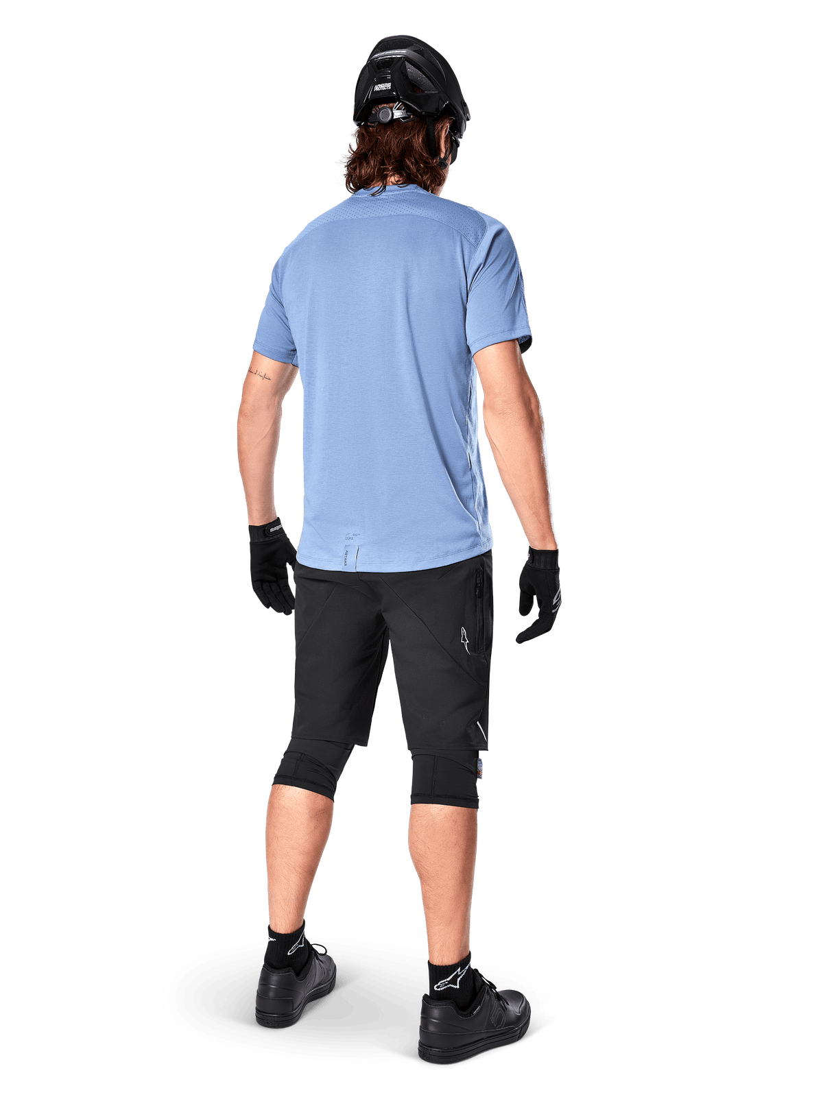 Jersey de manga corta Alpinestars A-Dura Dri Astar, Infinity Blue, vista posterior, combinado con pantalones cortos de bicicleta de montaña y casco negros, ropa técnica de ciclismo con tejido que absorbe la humedad y parte trasera más larga