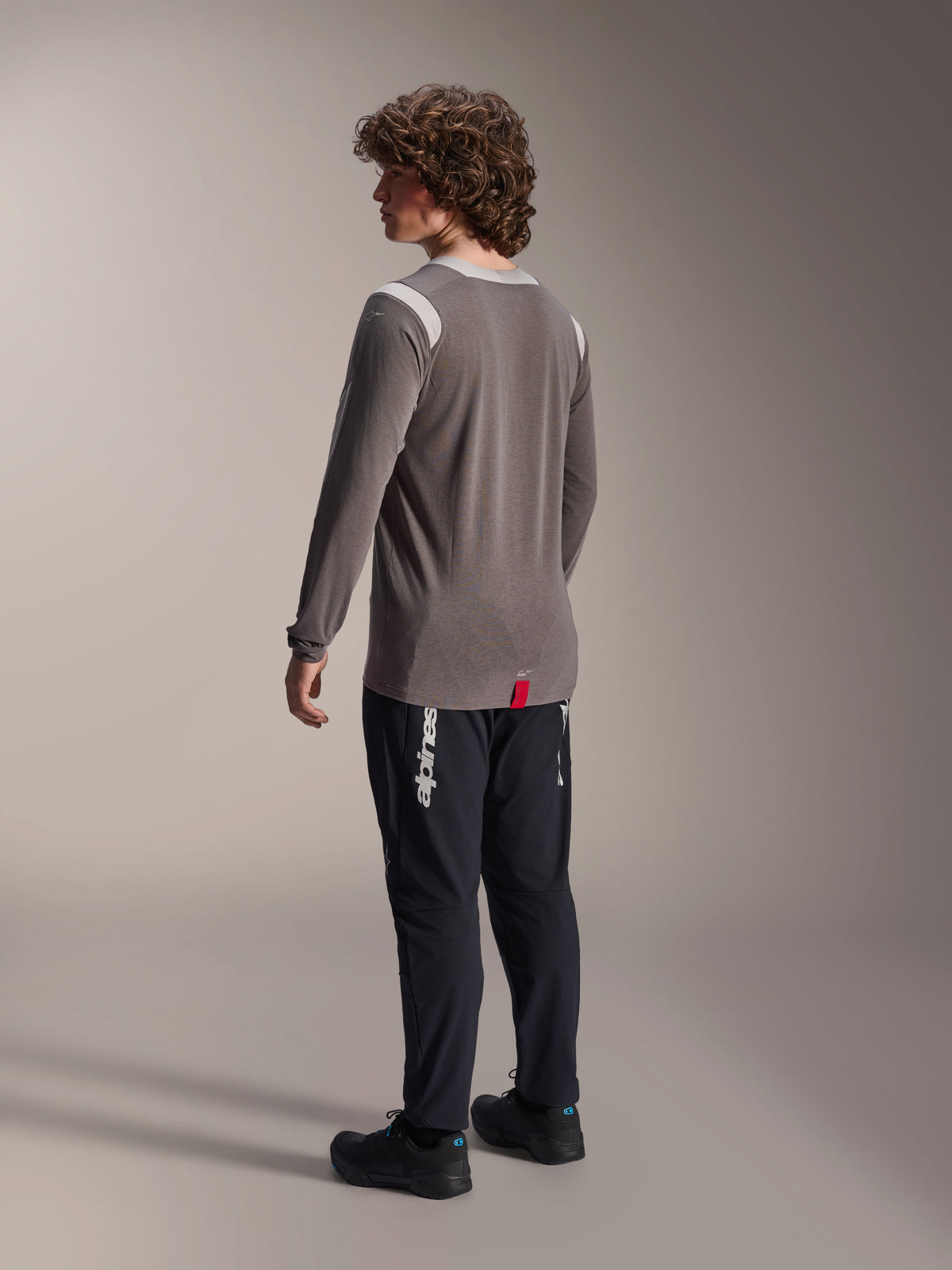 Jersey de manga larga Alpinestars A-Dura Dri-Wool en gris combinado con pantalones A-Dura Elite en negro, vista trasera del modelo, con logotipo blanco de Alpinestars en la pierna, equipo técnico de bicicleta de montaña para conducción fuera de pista