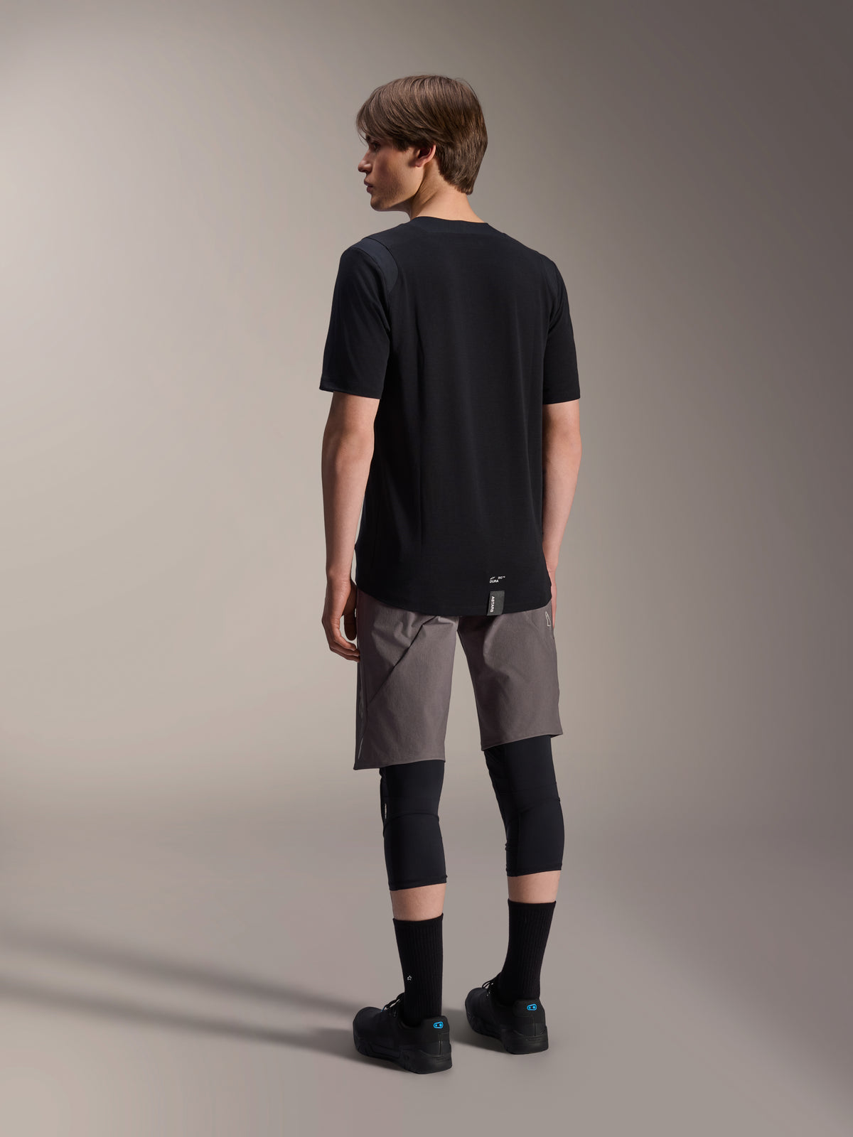 Alpinestars A-Dura Dri Wool Short Sleeve Jersey and A-Dura Elite Shorts, black and dark gray mountain bike apparel, worn with black knee guards and socks, back view of cycling gear for off-road performance