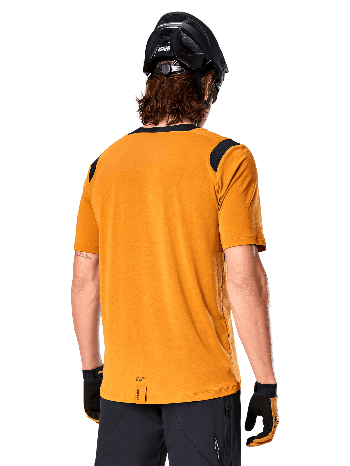 Alpinestars A-Dura Dri Wool Jersey de manga corta, oro oscuro, vista trasera de un hombre usando el jersey de manga corta con paneles de malla negra en los hombros, combinado con un casco de MTB negro y guantes, equipamiento de ciclismo de montaña de ajuste regular.