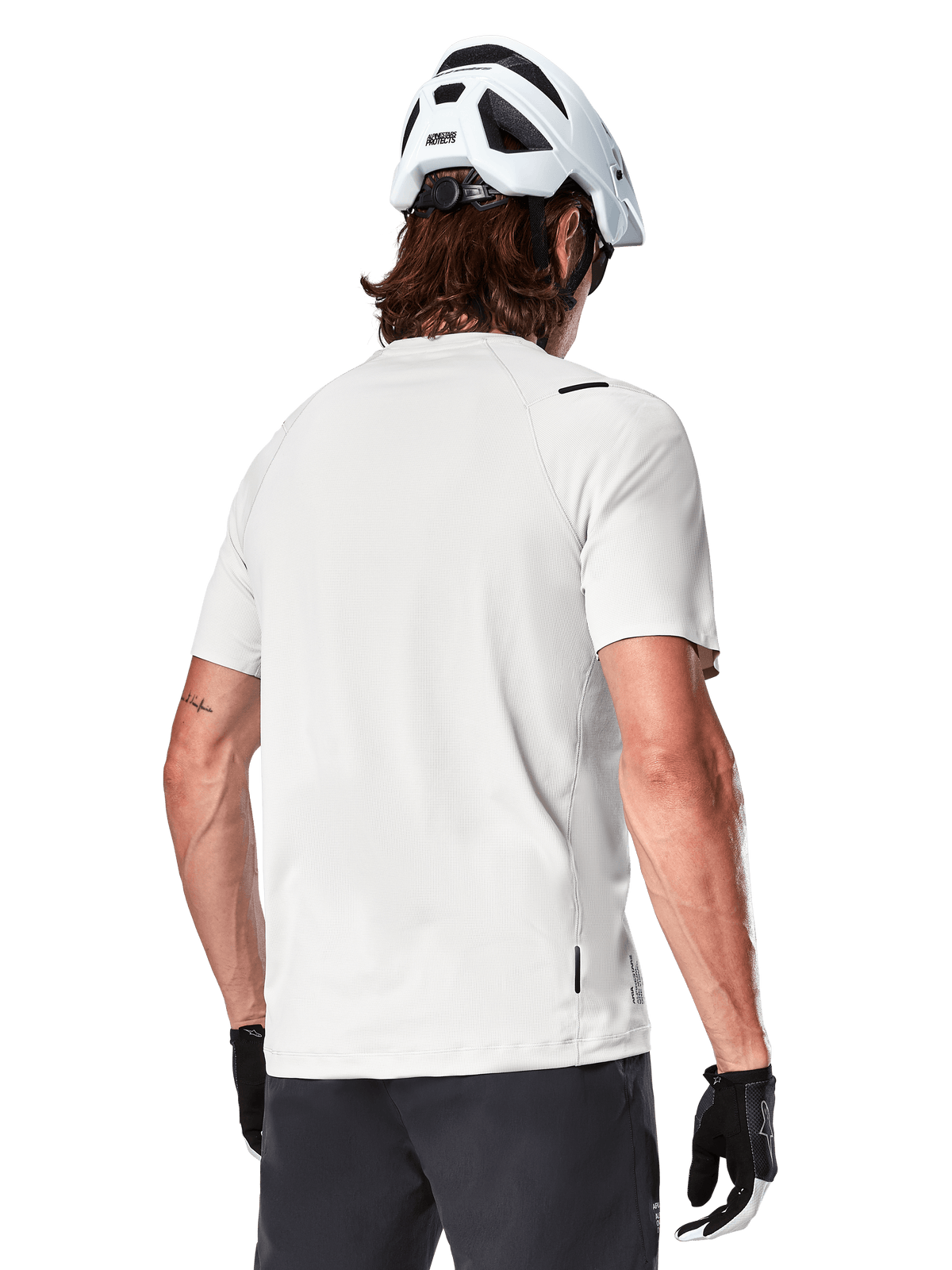 Alpinestars A-Aria Astar Jersey, manga corta, blanco (White Dove), vista trasera de este jersey de ciclismo de montaña ligero y transpirable, usado con casco blanco y guantes de ciclismo negros, con una parte trasera más larga para mayor cobertura