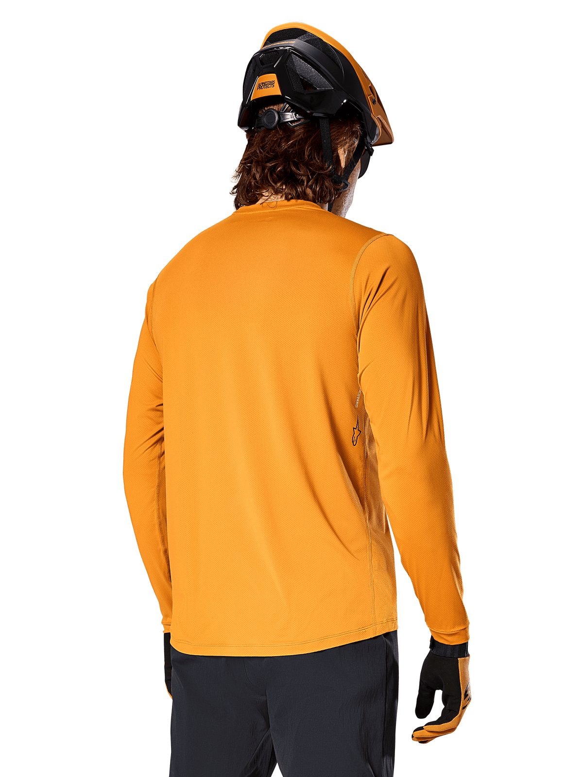 Alpinestars Jersey de manga larga A-Dura Rocker, Oro Oscuro, vista posterior del ciclista con casco de MTB negro y naranja, pantalones oscuros y guantes a juego, ropa de ciclismo de montaña de rendimiento casual