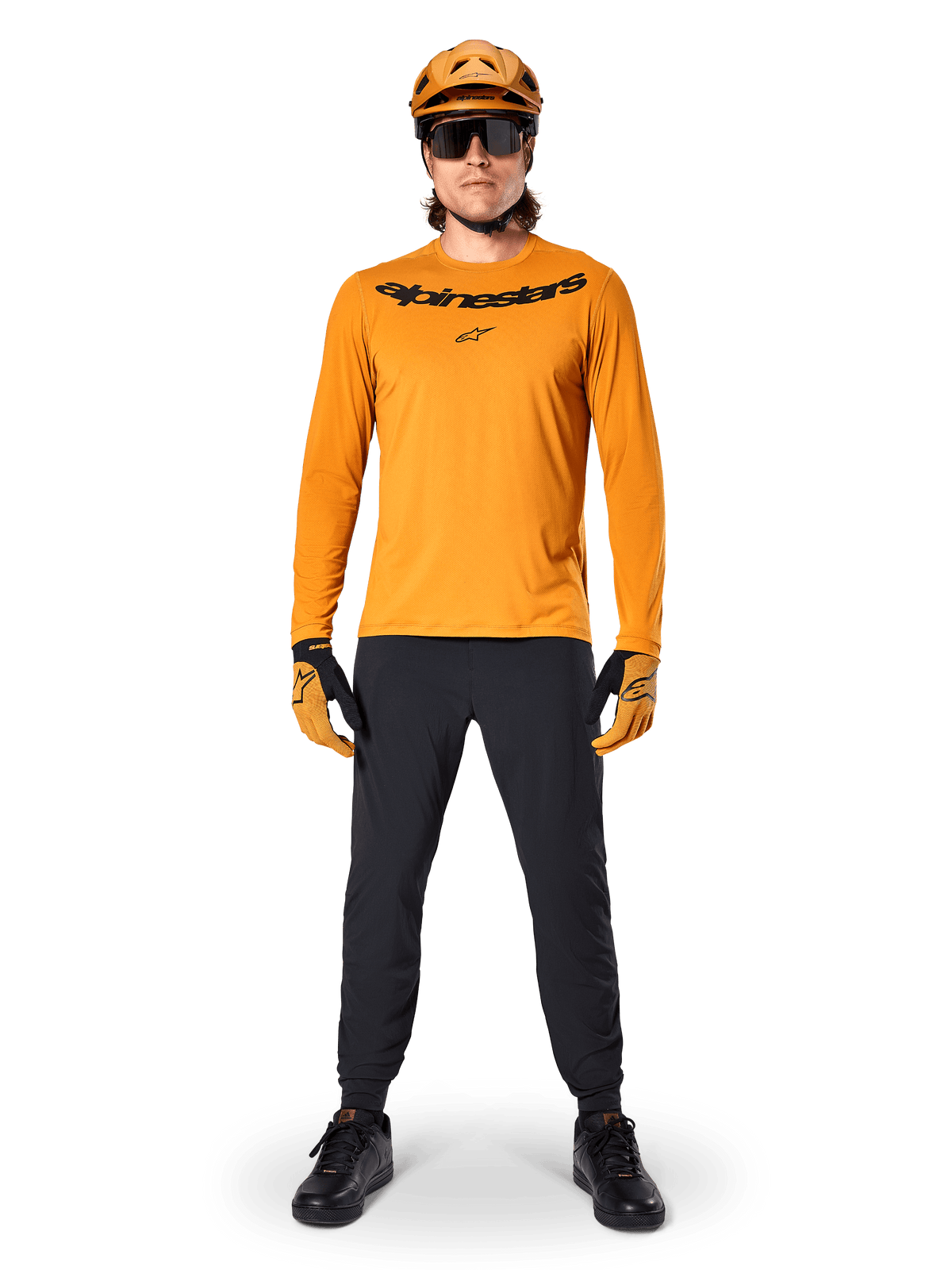 Jersey de manga larga Alpinestars A-Dura Rocker en color Dark Gold, con logotipo serigrafiado en negro en el pecho, usado con un casco de MTB dorado a juego, gafas de sol negras y pantalones negros, equipamiento profesional de ciclismo de montaña