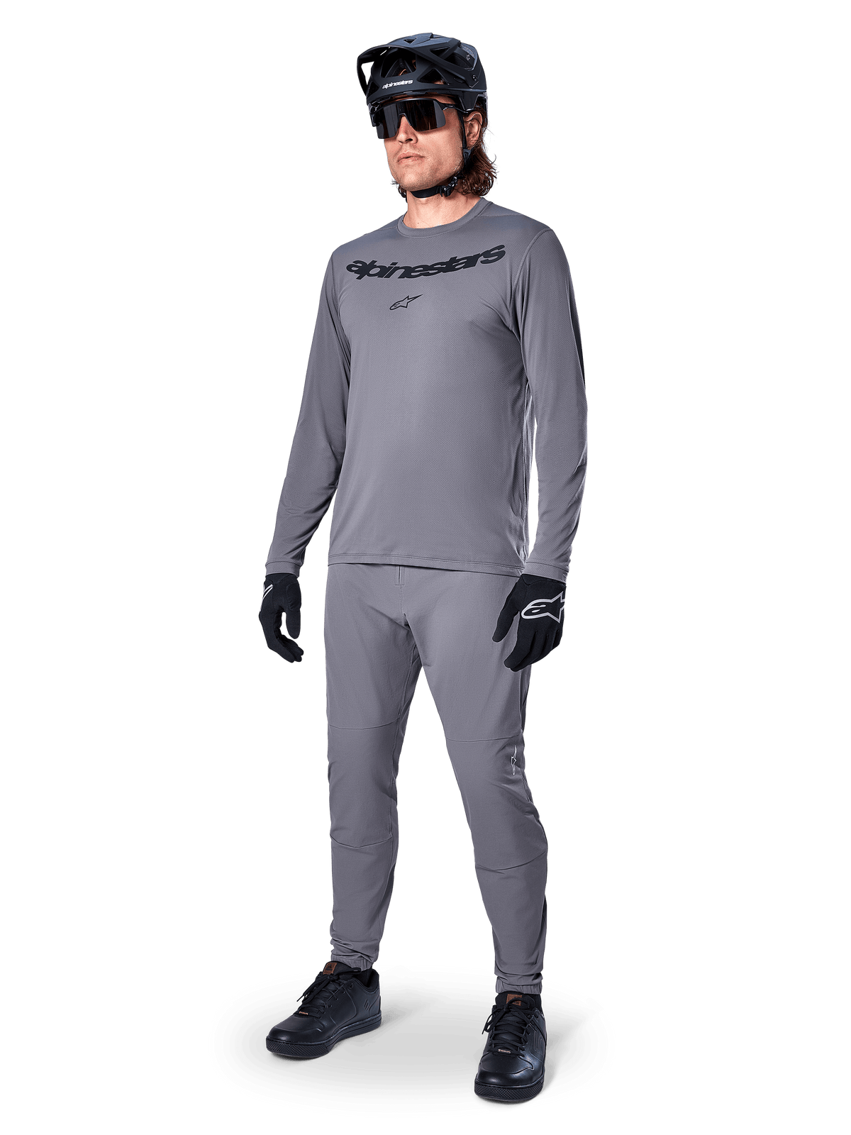 Alpinestars A-Dura Rocker Jersey - Long Sleeve, gris oscuro, usado por un modelo con pantalones grises a juego, casco de bicicleta de montaña negro, gafas de sol y guantes, estilo casual de MTB para conducción fuera de pista
