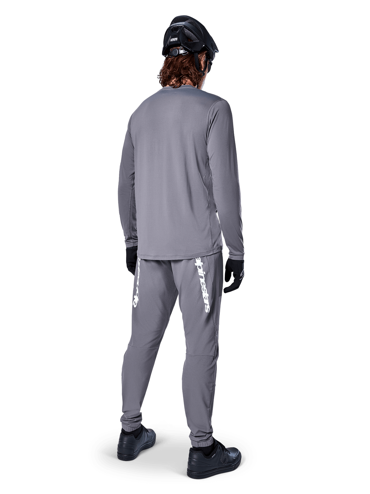 Jersey de manga larga Alpinestars A-Dura Rocker, gris oscuro, vista trasera del modelo luciendo pantalones de MTB grises a juego, casco negro y guantes negros, diseño de ropa profesional para bicicleta de montaña