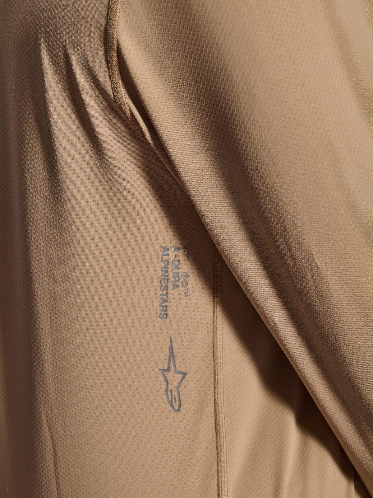 Jersey de manga larga Alpinestars A-Dura Astar, camiseta de ciclismo MTB, marrón, primer plano que muestra la textura del tejido jacquard, logotipo de Astars y marca denominativa A-Dura impresos, ropa técnica para bicicleta de montaña