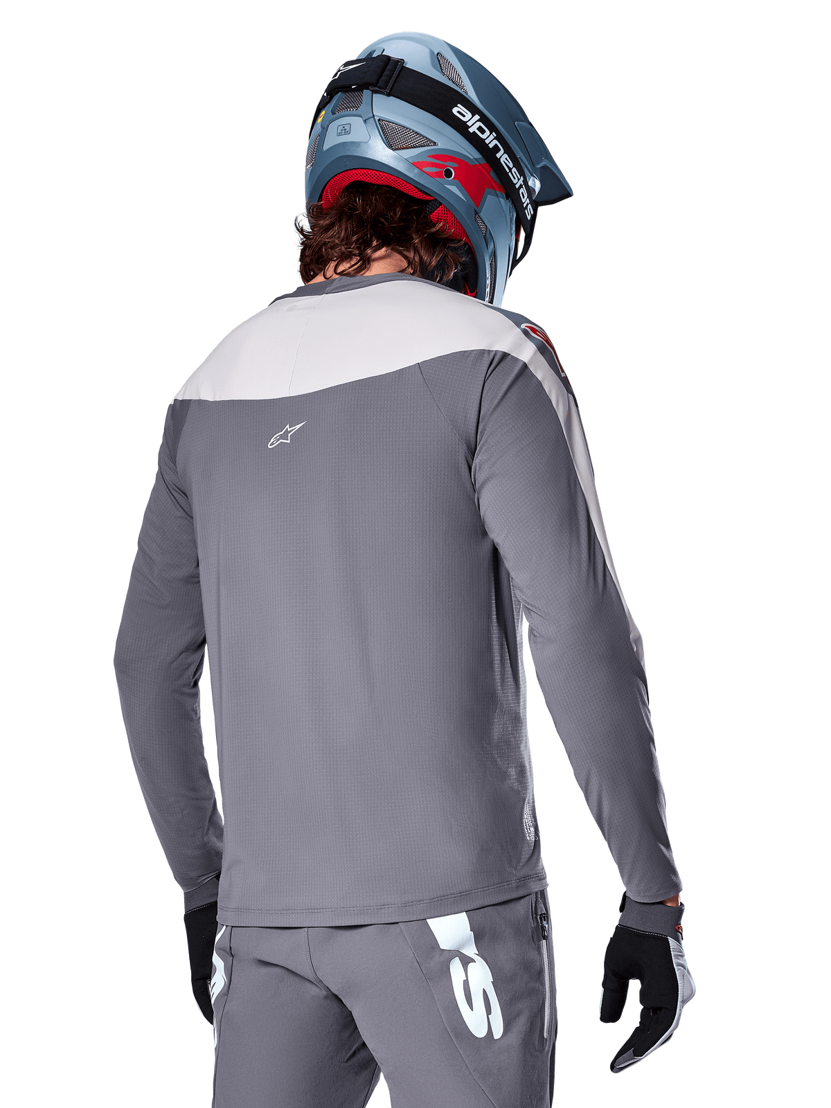 Alpinestars A-Supra Race Jersey, jersey de MTB de manga larga en gris oscuro y gris claro, vista posterior que muestra el ajuste de rendimiento y el logotipo Astar, usado con pantalones grises a juego y un casco azul de bicicleta de montaña, diseñado para ciclismo de montaña.