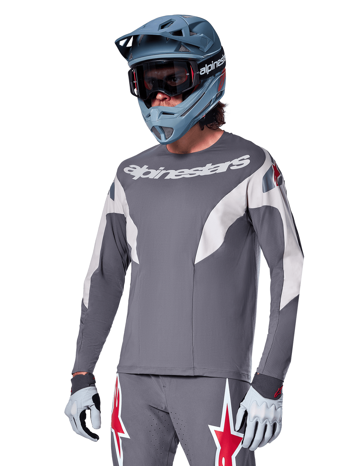 Alpinestars A-Supra Race Jersey de manga larga, gris oscuro con detalles blancos y rojos, gráficos de estilo de carreras, usado con pantalones grises a juego, casco integral azul y guantes blancos, equipo profesional de MTB y descenso
