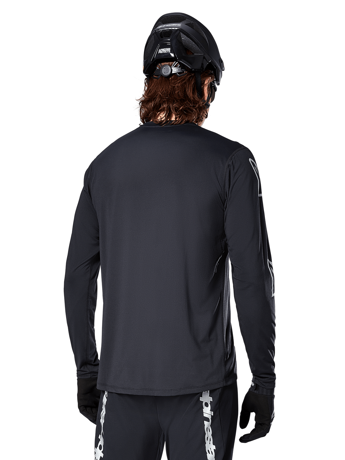 Jersey de manga larga Alpinestars A-Dura Switch, negro, vista trasera de un ciclista con casco de MTB y guantes negros, con tejido jacquard técnico y parte trasera más larga para conducción off-road
