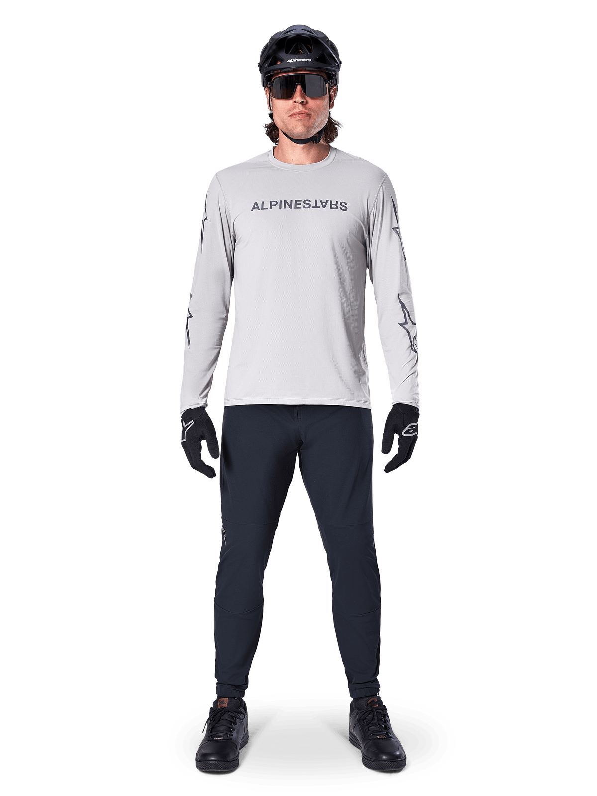 Jersey de manga larga Alpinestars A-Dura Switch en gris claro, con un logotipo estilizado en el pecho, combinado con pantalones negros, casco y guantes, ropa de alto rendimiento para ciclismo de montaña fuera de pista