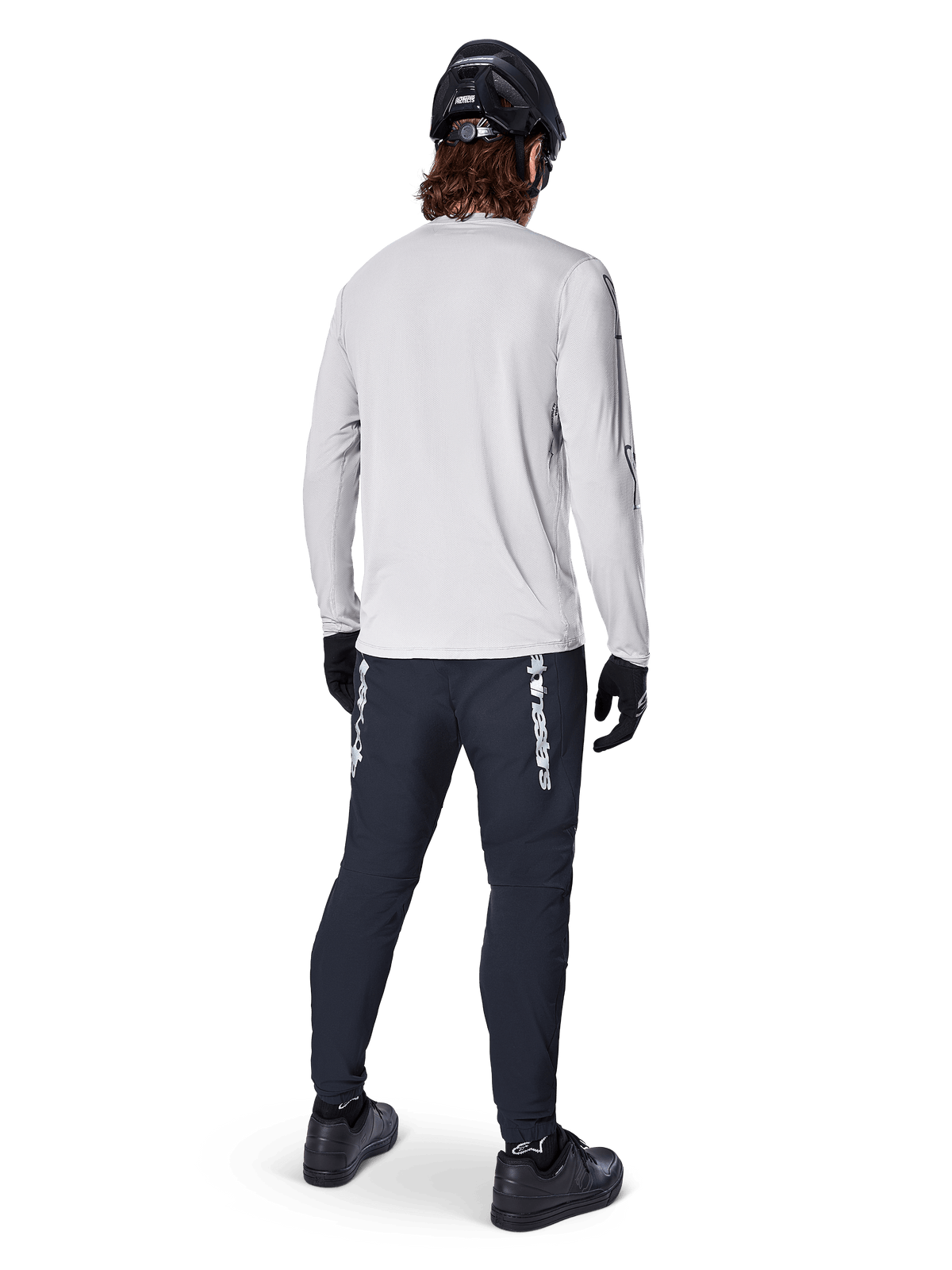 Alpinestars A-Dura Switch Jersey de manga larga, gris claro, vista posterior de un ciclista con pantalones de ciclismo negros, casco y guantes, equipamiento de alto rendimiento para MTB con parte trasera más larga