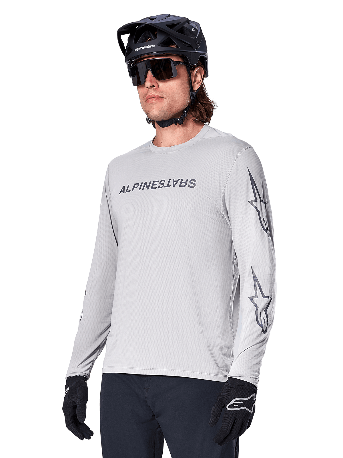 Alpinestars A-Dura Switch Long Sleeve Jersey, camiseta de manga larga para bicicleta de montaña, gris claro, serigrafía negra de la marca en el pecho y logotipos de estrellas en las mangas, usado con casco negro de MTB, gafas de sol oscuras y guantes negros, equipamiento deportivo para ciclismo off-road