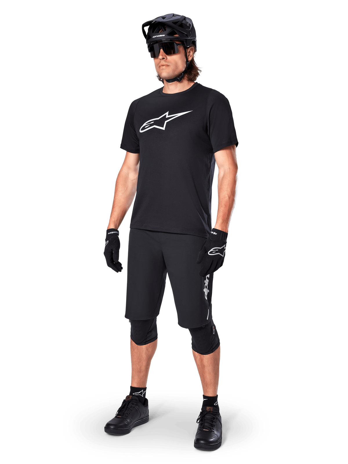 Ciclista de montaña con el Jersey de manga corta Alpinestars A-Dura Dri Oscar en Negro Reflectante, con un gran logotipo blanco en el pecho, combinado con pantalones cortos de MTB, guantes y casco negros a juego, ropa técnica de ciclismo para rendimiento off-road