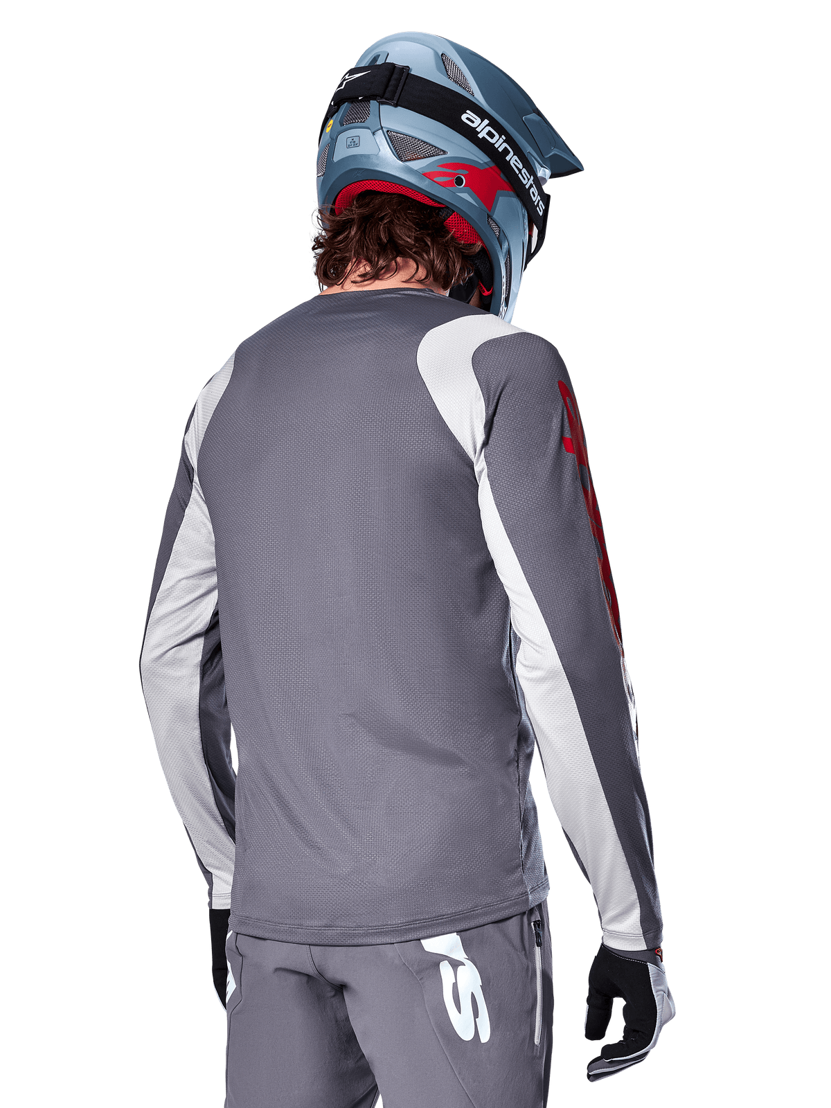 Jersey Alpinestars A-Supra Astar de manga larga, gris oscuro con paneles en gris claro en hombros y brazos, vista trasera del ciclista con casco integral de MTB azul y pantalones grises, ropa de ciclismo MTB de alto rendimiento