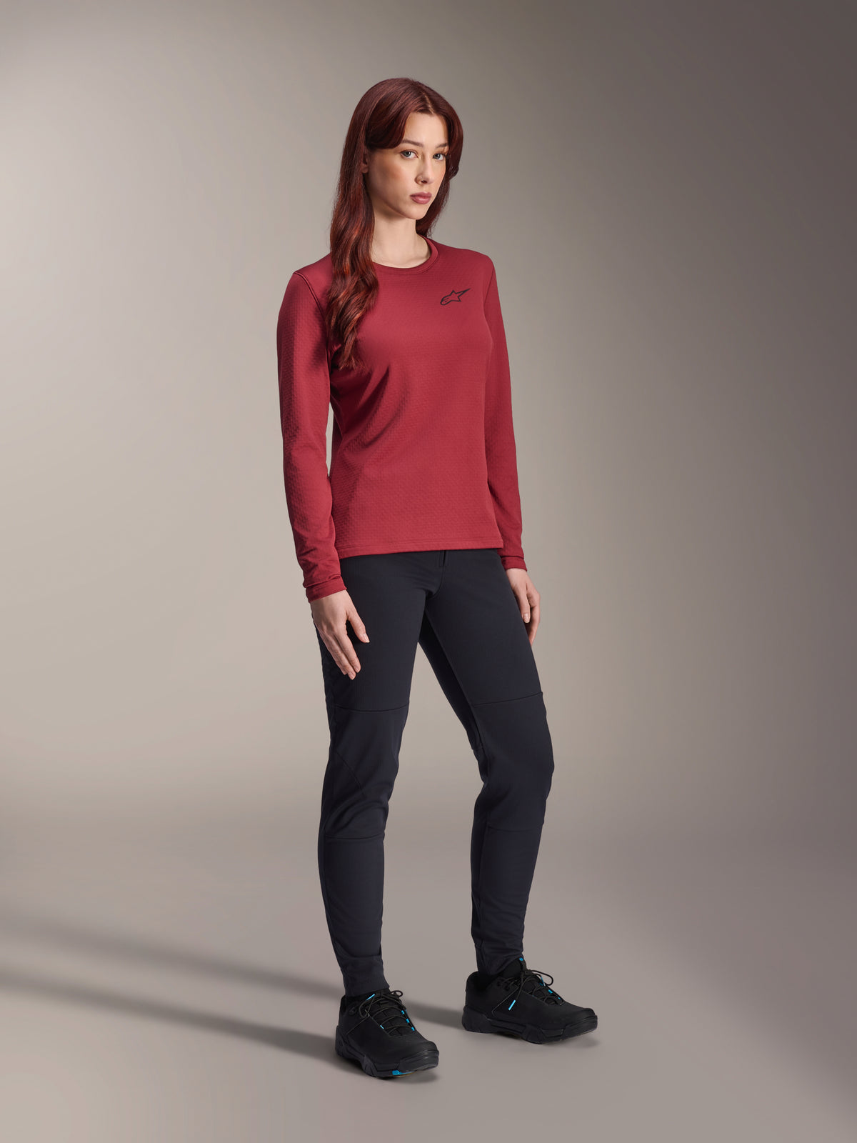 Alpinestars Stella A-Dura Thermal Jersey, jersey de ciclismo de montaña de manga larga para mujer, color borgoña, usado con pantalones deportivos negros y calzado negro, cuello redondo con pequeño logo negro en el pecho, diseño funcional de ajuste regular para ciclismo de montaña