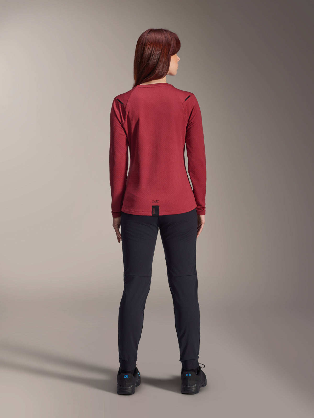 Pantalones térmicos Alpinestars Stella A-Dura, pantalones de ciclismo de montaña para mujer, negros, combinados con un jersey térmico de manga larga color burdeos, vista trasera que muestra el ajuste técnico y la construcción para ciclismo en climas fríos.