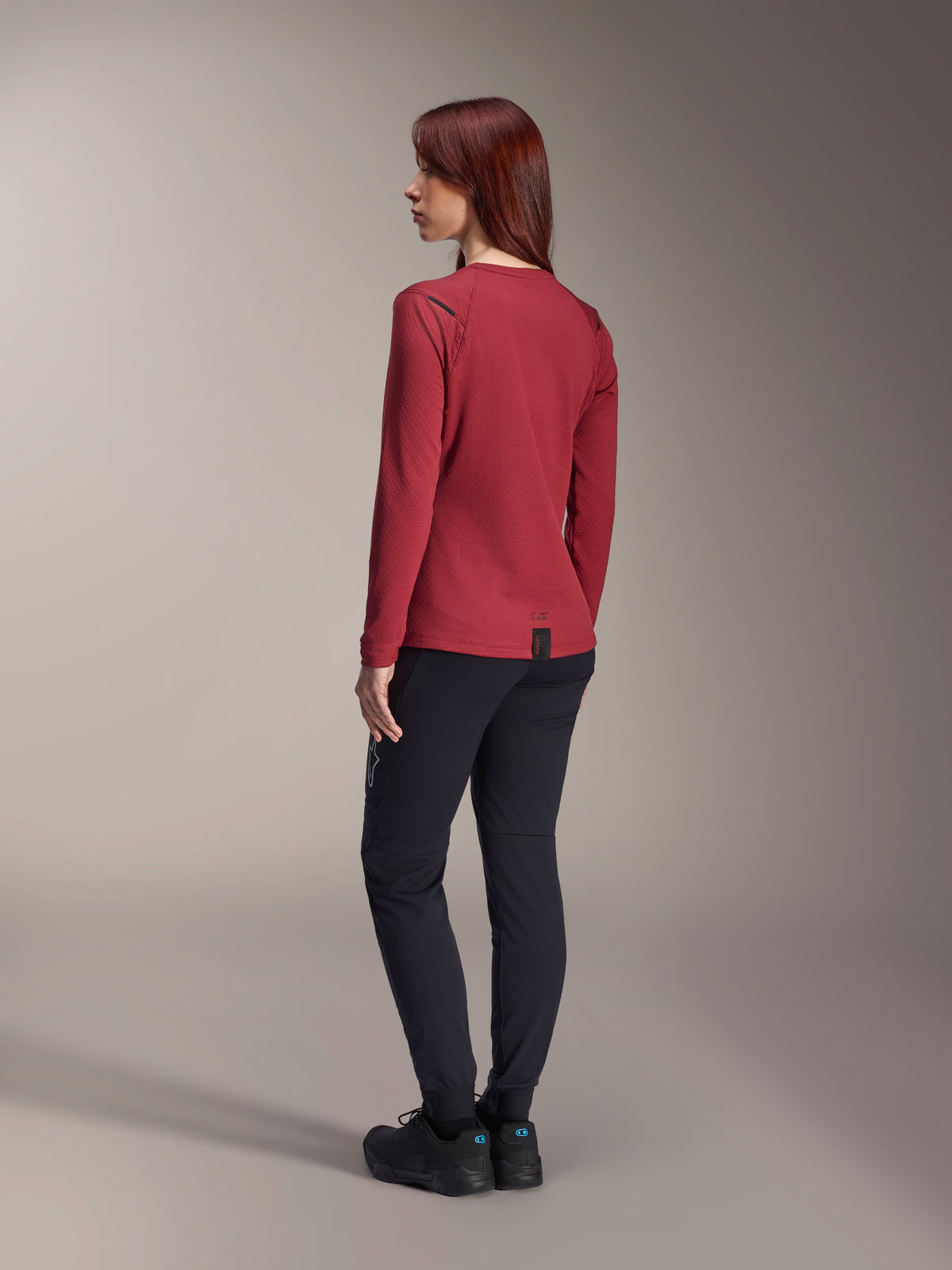 Mujer con pantalones térmicos Alpinestars Stella A-Dura en negro, combinados con un jersey térmico rojo de manga larga y calzado negro, vista trasera, ropa de ciclismo de montaña para montar en climas fríos.