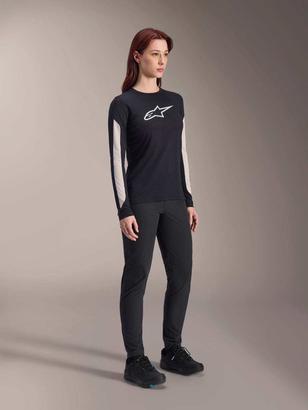 Mujer con equipamiento de MTB de Alpinestars, jersey Stella A-Dura Elite negro con logotipo blanco en el pecho y paneles en las mangas, pantalones Stella A-Dura negros, zapatillas de ciclismo negras con detalles azules, equipamiento de alto rendimiento completo para mountain bike