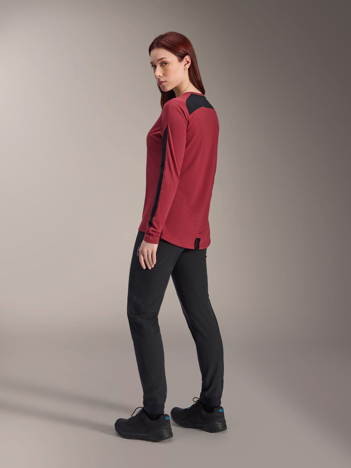 Alpinestars Stella A-Dura Dri Astar, jersey de manga larga para mujer, color granate y negro, usado con pantalones de MTB y zapatillas negras, vista de perfil lateral trasera, tejido drirelease® reciclado con paneles de malla, prenda técnica de ciclismo de montaña.
