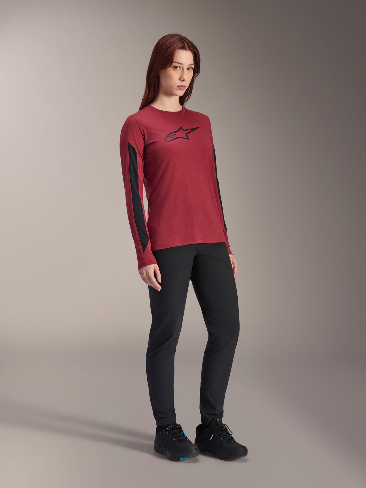 Jersey de manga larga para mujer Alpinestars Stella A-Dura Dri Astar, rojo borgoña con logo negro en el pecho y paneles de malla negros en las mangas, usado con pantalones técnicos negros y zapatillas de ciclismo negras, ropa de ciclismo de montaña de alto rendimiento para mujer