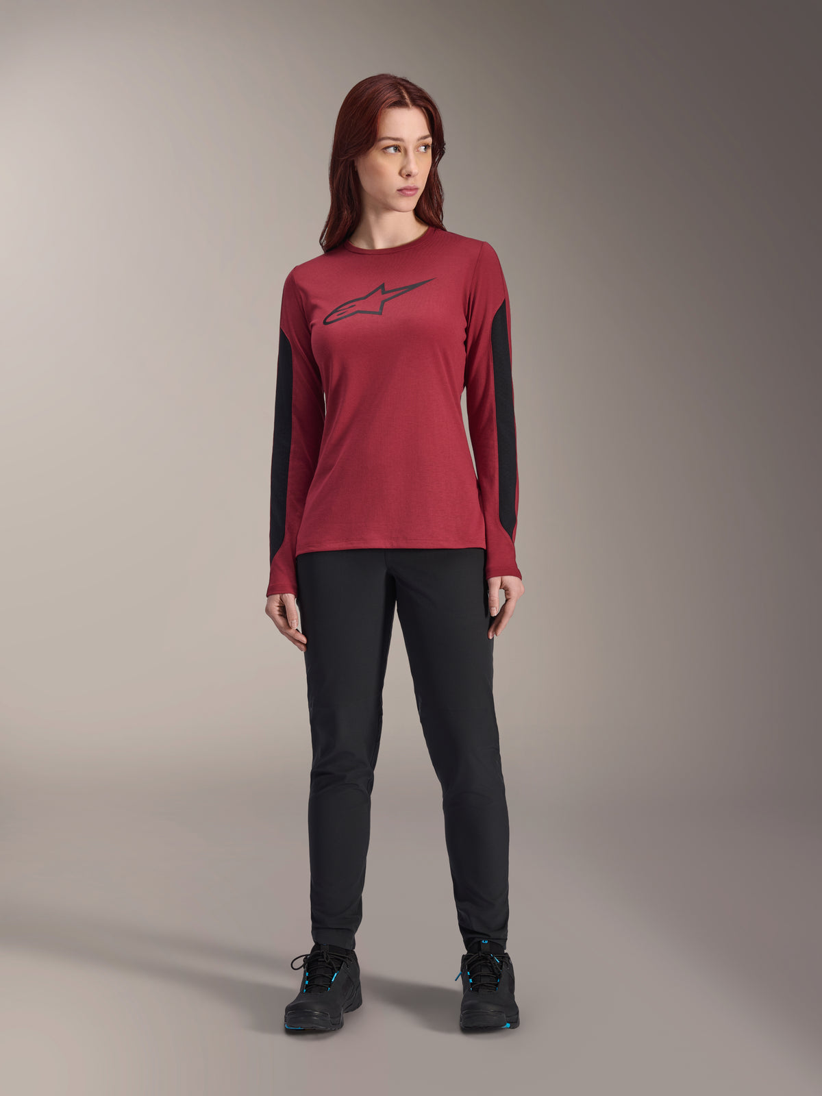 Jersey Alpinestars Stella A-Dura Dri Astar de manga larga para mujer en color burdeos, con un logotipo Astars negro en el pecho y paneles de malla negros en las mangas, combinado con pantalones técnicos negros y calzado deportivo, ropa de alto rendimiento para ciclismo de montaña.
