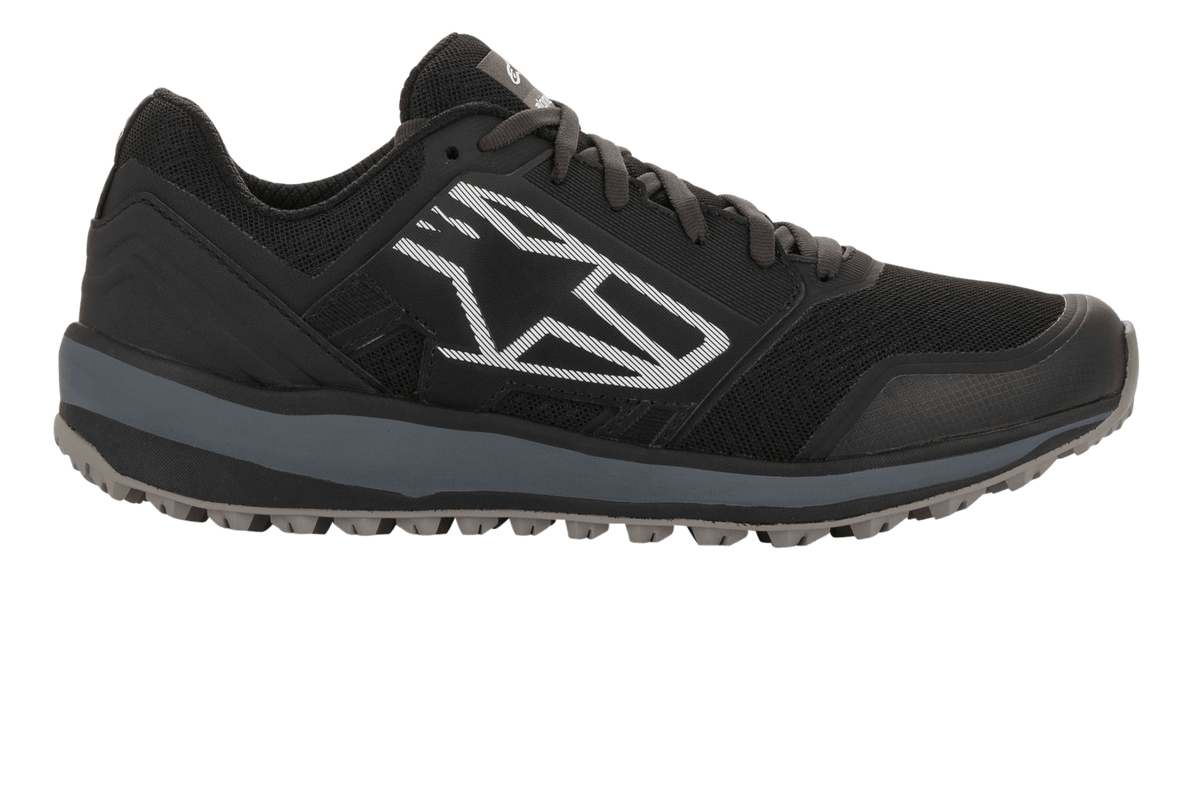 Alpinestars Meta Trail Shoes, zapatillas de running de alto rendimiento, negro y gris oscuro, perfil lateral con un gran logotipo geométrico de Astars en blanco, parte superior de malla con entresuela gris y suela de goma con tacos, calzado casual para paddock de automovilismo