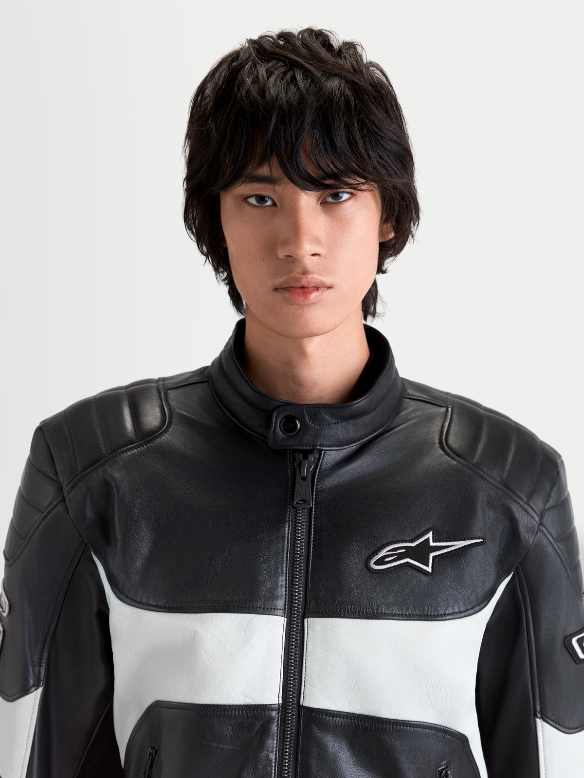Alpinestars Revern Leather Jacket, men's urban motorcycle leather jacket in black and metal gray, front close-up view on a model showing full-grain leather construction, biker collar, and white Alpinestars logo branding.