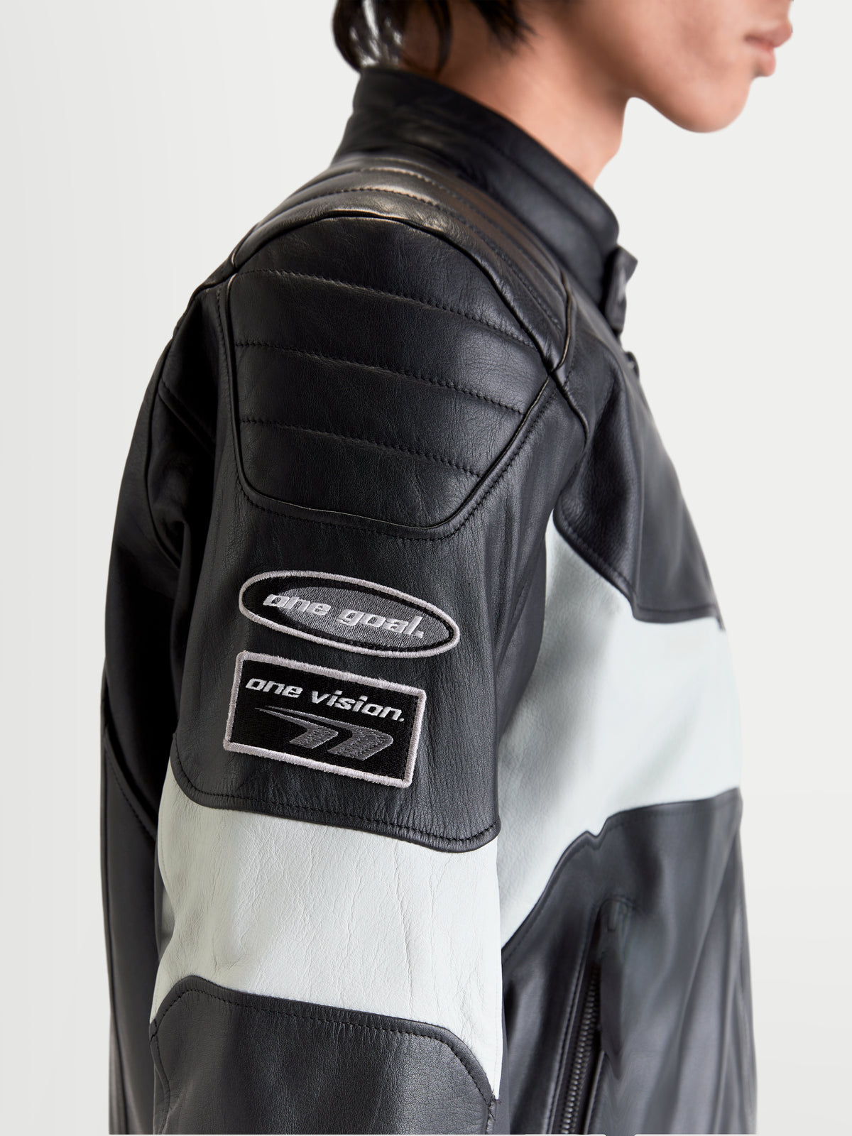 Alpinestars Revern Leather Jacket, men's urban motorcycle leather jacket in black and metal gray, side profile close-up showing heritage-inspired branding patches on the sleeve and distressed bovine leather construction worn by a model.
