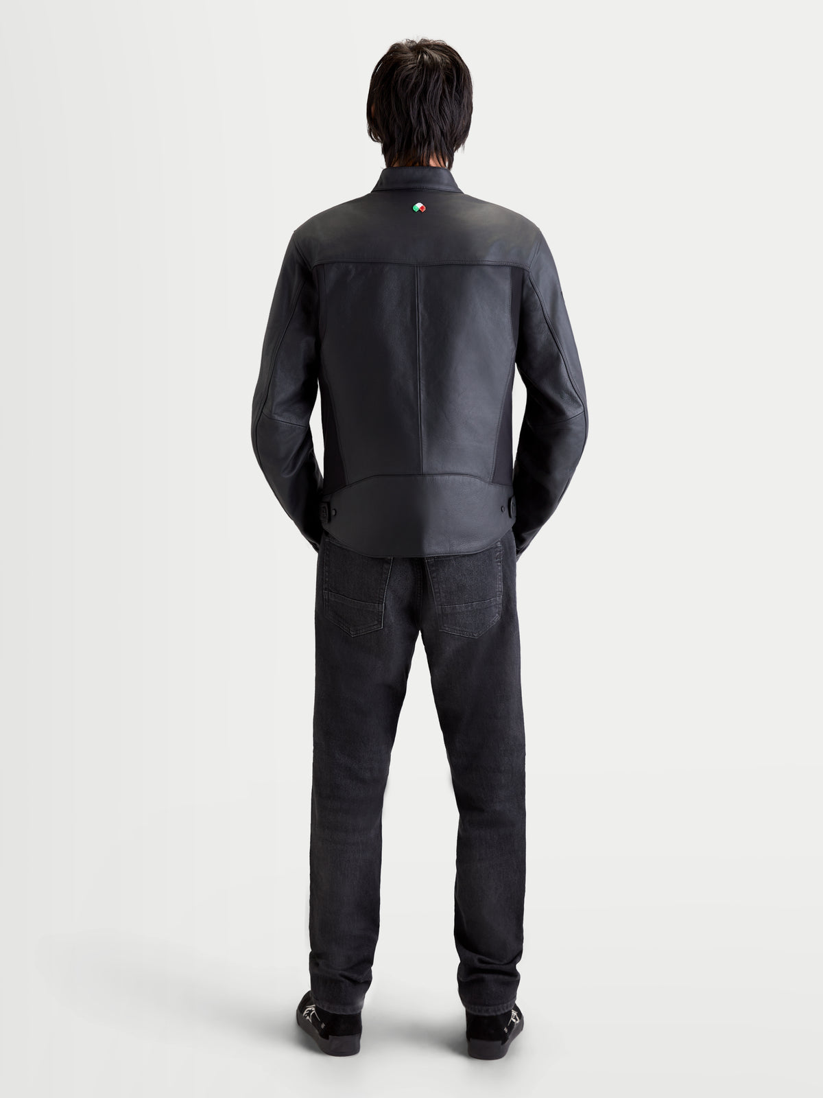 Alpinestars Maver X Chaqueta de cuero, chaqueta de moto urbana contemporánea para hombre en color negro, vista trasera de un modelo con jeans y zapatos oscuros a juego, mostrando la construcción de cuero premium y el detalle del cuello