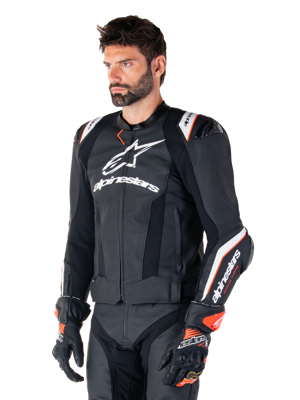 Modelo masculino vistiendo la chaqueta de cuero Alpinestars Missile V3 Ignition, negra con detalles en blanco y naranja, con logotipos blancos prominentes, secciones de cuero perforado y protecciones en los hombros, combinada con guantes de carreras para un look deportivo de competición