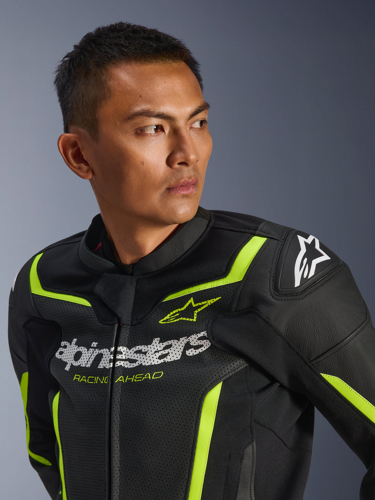 Chaqueta de cuero Alpinestars GP Force V2 Air, negro y amarillo flúor, chaqueta deportiva de moto perforada con logotipo blanco en el pecho y el texto 'Racing Ahead', detalles en neón y deslizadores protectores en los hombros, lucida por un modelo masculino.