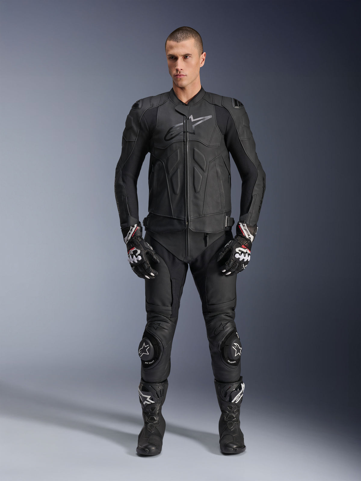 Alpinestars Chaqueta de Cuero Dusk, chaqueta de moto deportiva para hombre, negra, cuero bovino, usada por un modelo con equipo de carreras completo