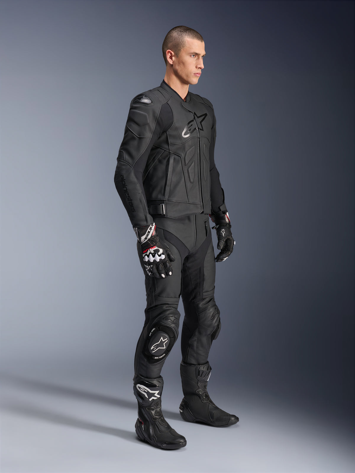 Pantalones de cuero Alpinestars Missile V3, combinados con una chaqueta de cuero negra, guantes y botas a juego, con deslizadores de rodilla y un ajuste de competición aerodinámico, equipamiento de protección integral para moto en color negro para pista y carretera.