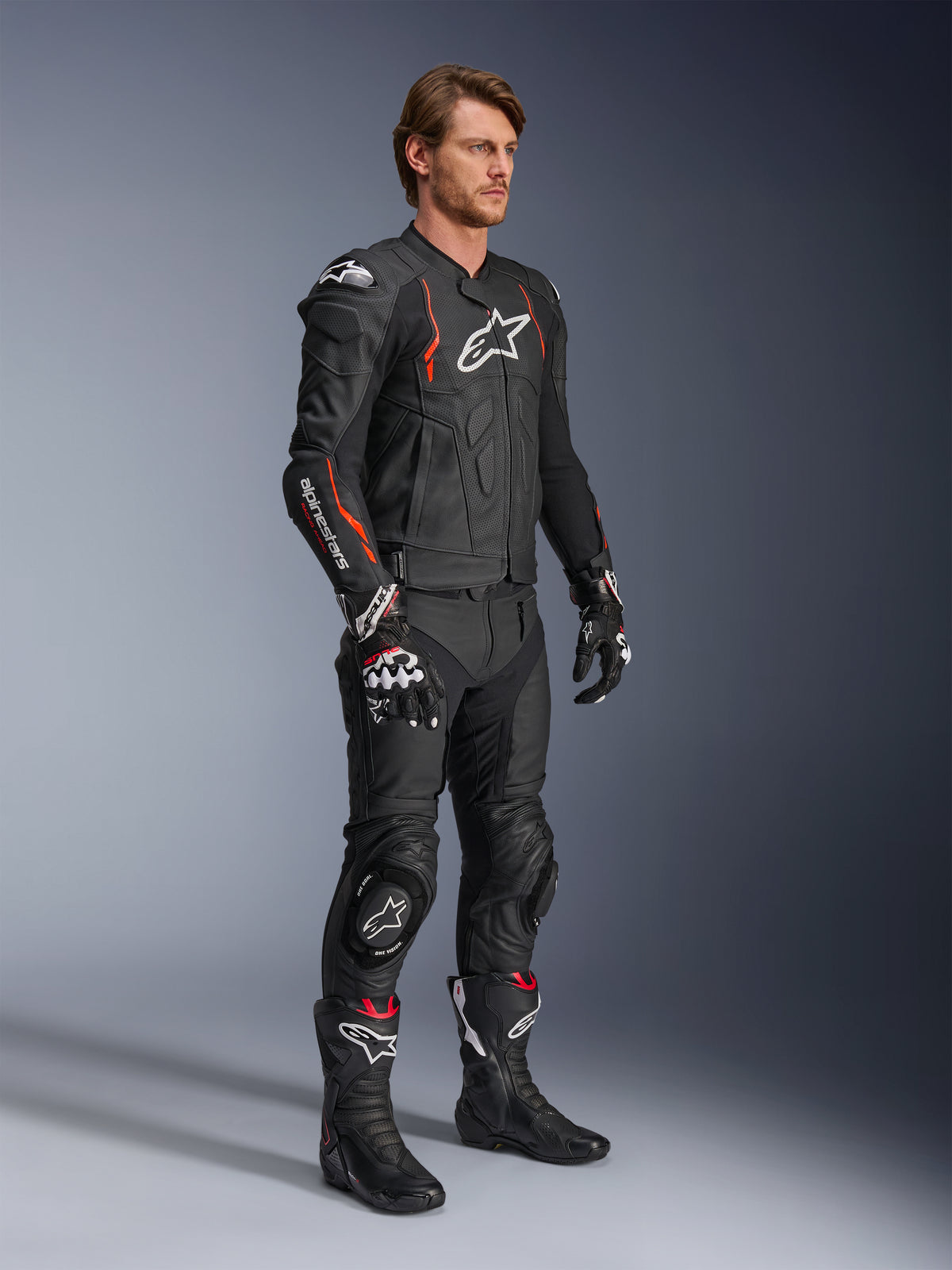 Chaqueta de cuero Alpinestars Dusk Airflow, Negro Rojo Flúor, usada como parte de un equipamiento completo de motociclismo con pantalones de cuero, guantes y botas a juego, con construcción de cuero perforado y detalles deportivos