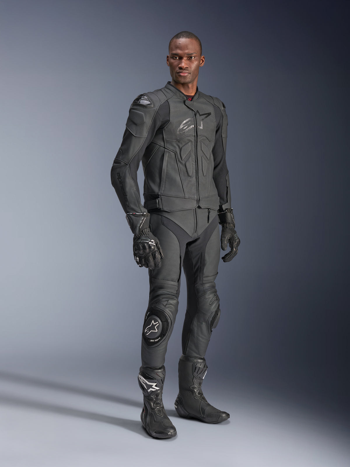 Chaqueta de cuero Alpinestars Dusk Airflow, Negro Negro, vestida por un piloto con equipamiento técnico completo que incluye pantalones de cuero, guantes y botas a juego, con paneles de cuero perforado para ventilación y armadura integrada para conducción deportiva de motocicletas.