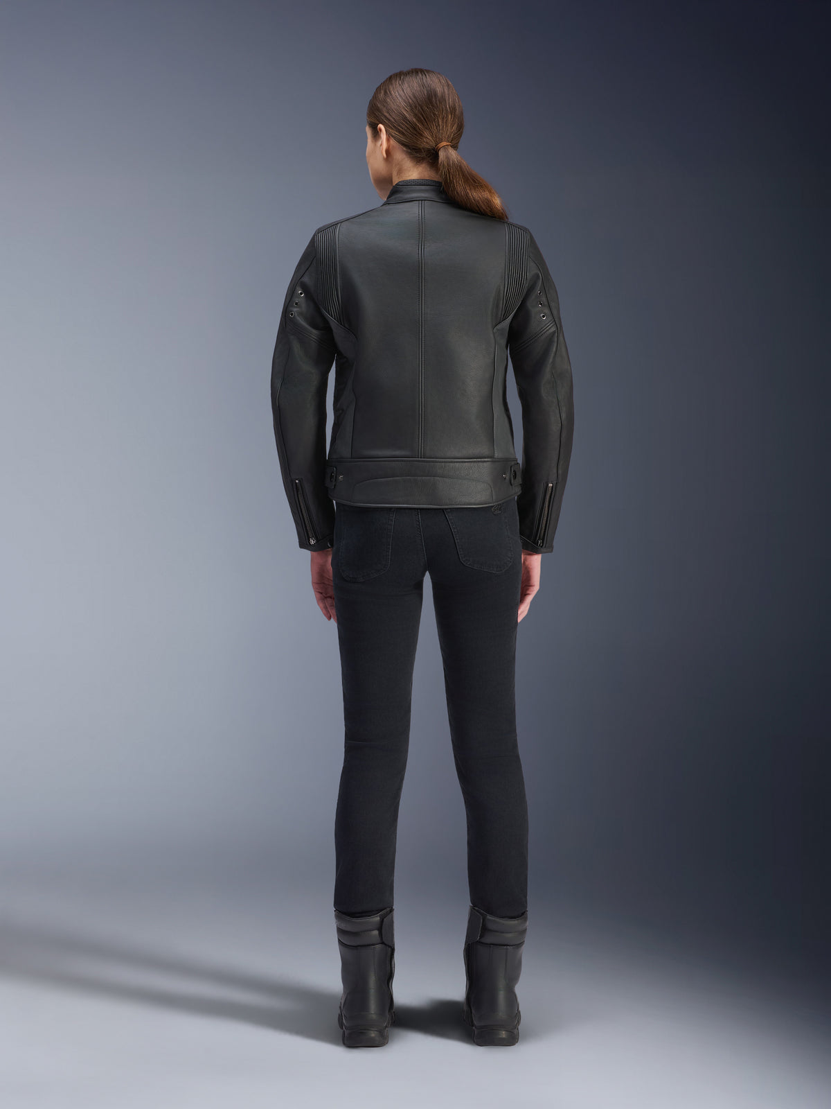 Alpinestars Stella Dyno Leather Jacket, chaqueta de moto para mujer, negro, vista trasera que resalta la confección entallada en cuero bovino, diseño minimalista de herencia, combinada con pantalones de montar y botas negros para un look de moto urbano