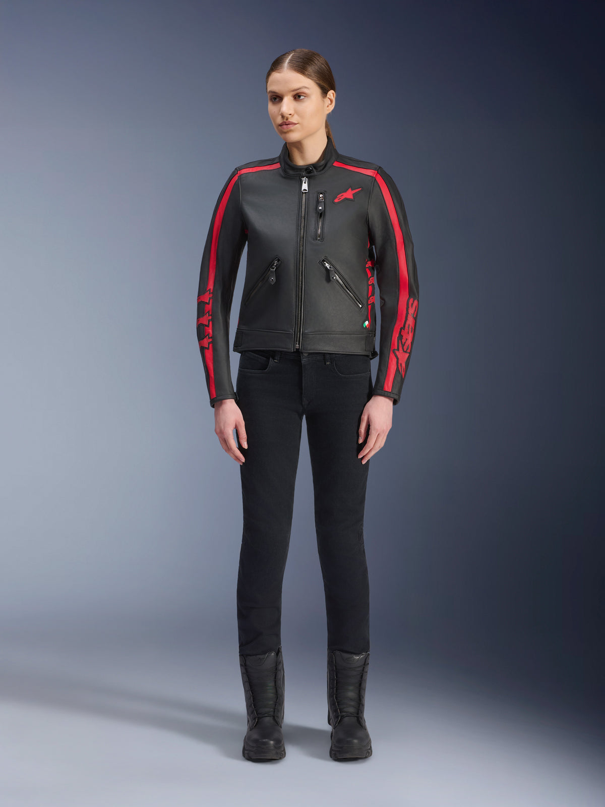 Chaqueta de cuero Alpinestars Stella Dyno, chaqueta de moto para mujer, negra y roja, con franjas rojas de competición en hombros y mangas, logo de estrella roja en el pecho, usada con pantalones negros de corte ajustado y botas, cuero de bovino de primera calidad con un diseño de herencia moderno