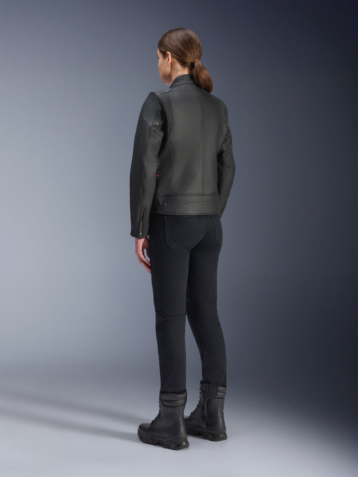Chaqueta de cuero Alpinestars Stella Dyno, chaqueta de moto para mujer, negro y rojo (Black Haute Red), vista trasera, usada con pantalones de conducción negros y botas negras, acabado de cuero de primera calidad con estilo herencia